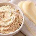 Schale mit gemahlenen Mandeln, Naturholzlöffel und cremige Peeling-Textur auf Leinentuch