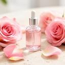 Rosenwasser-Flakon neben frischen Damaszener-Rosen auf einem hellen Steintisch